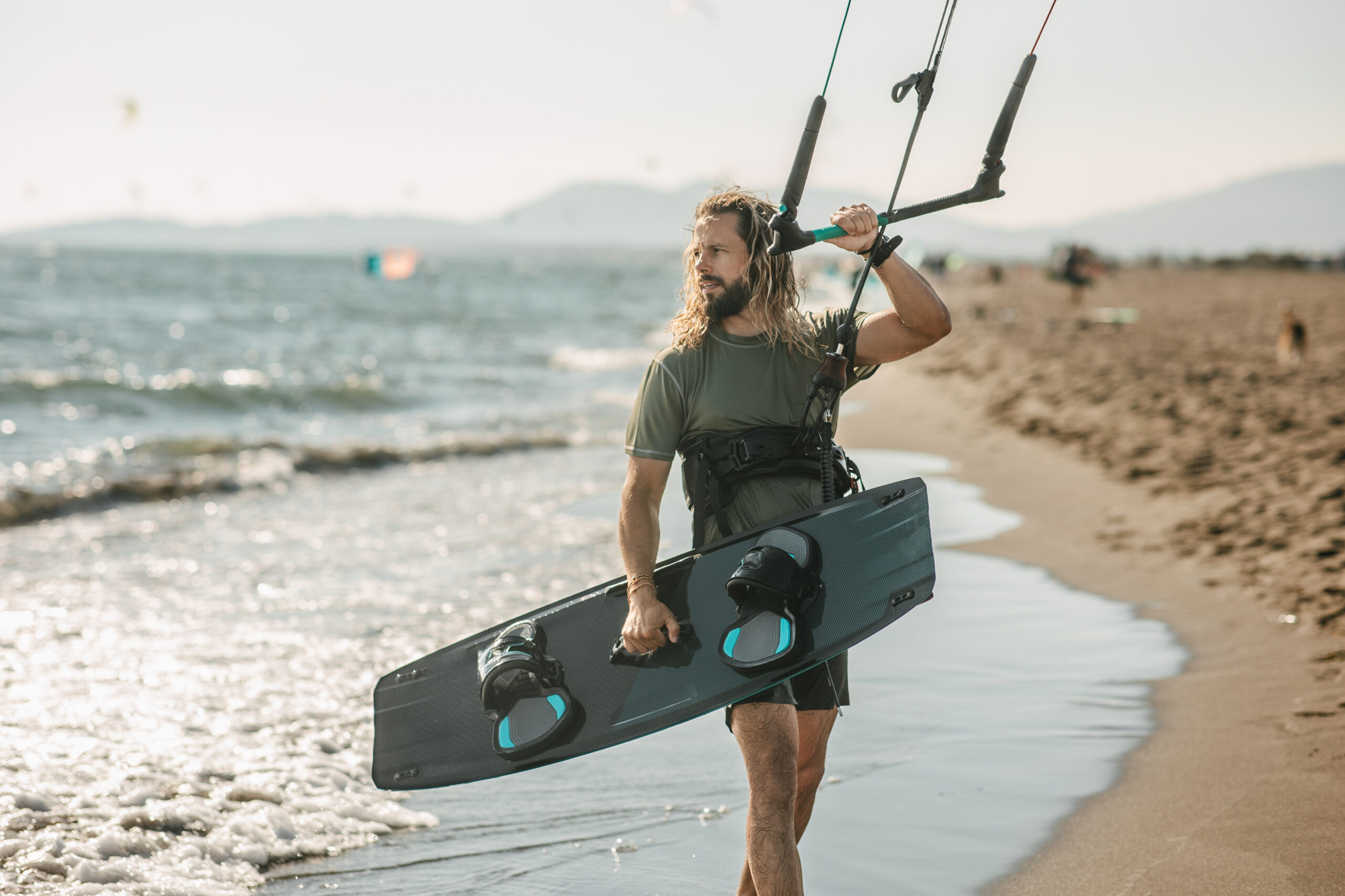 Man walking with kitesurfing equipment on beach.