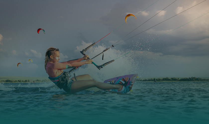 Kiteboarder riding waves under cloudy sky.